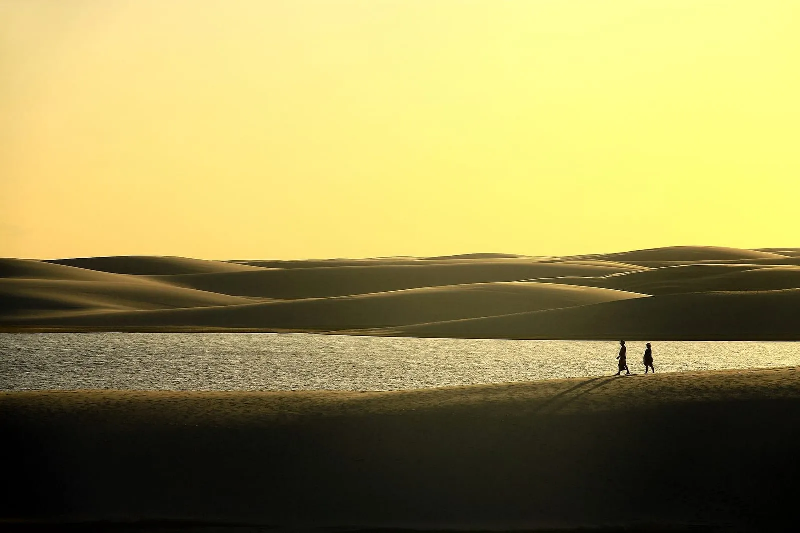 Casal caminha nas dunas dos Lençóis Maranhenses ao pôr do sol